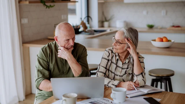 Elderly couple sitting in the dining room with documents and a laptop